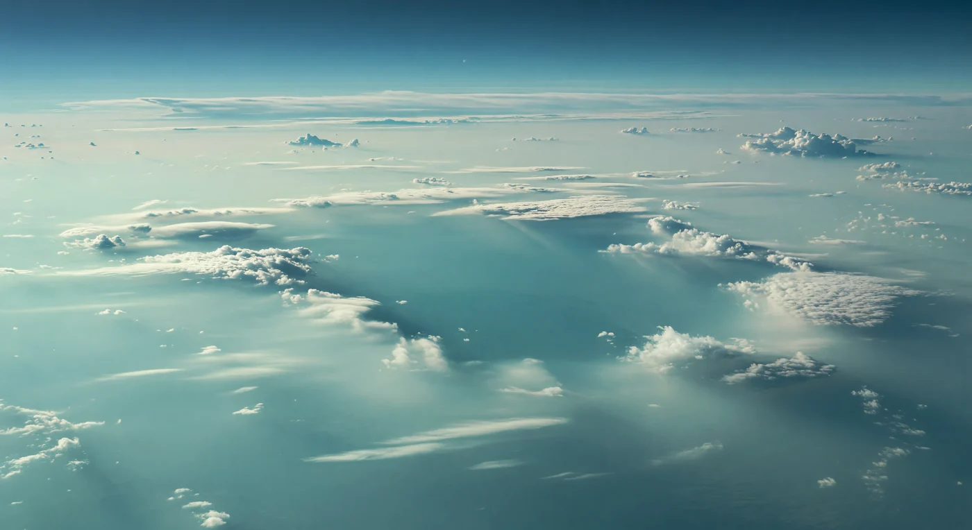 Ante ti se abre una inmensa grieta en las capas altas de nubes, una ventana irregular de escala continental que desciende hacia un estrato más profundo de azul verdoso intenso, donde la luz parece hundirse y apagarse. Sus bordes, delineados por bancos nubosos blanco plateado y cian muy pálido, muestran capas de aerosoles helados de metano y amoníaco que se deshilachan en una neblina lechosa bajo una iluminación fría, débil y casi sin sombras. No hay suelo ni horizonte sólido: solo llanuras ondulantes de nubes, velos estratificados y cúmulos convectivos suaves que revelan la naturaleza de este gigante de hielo, una atmósfera profunda donde la presión aumenta sin interrupción hacia fluidos exóticos bajo decenas de kilómetros de bruma. Muy arriba, el Sol apenas es un punto tenue perdido en el resplandor azul verdoso, y esa luz dispersa convierte la escena en un abismo silencioso de turquesa, aguamarina y azul profundo que hace sentir, al mismo tiempo, la delicadeza de las nubes y la escala abrumadora del mundo que las sostiene.