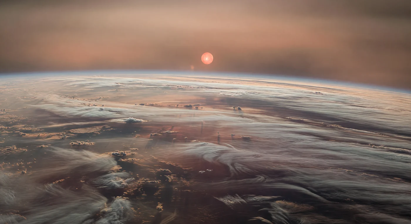 Sospeso negli strati superiori dell’atmosfera, lo sguardo abbraccia un immenso campo di nastri nuvolosi paralleli che seguono la curvatura del pianeta, tirati per migliaia di chilometri da venti superrotanti in filamenti color crema, teal grigiastro impolverato, malva spento, ruggine e carbone. Non esiste alcun suolo all’orizzonte: solo banchi di condensa torreggianti, corsie di foschia metallica e abissi di nubi più scure che suggeriscono la discesa verso un involucro profondo, caldo e ricco d’acqua in stato supercritico, dove pressione e temperatura cancellano ogni confine familiare tra gas e liquido. La luce obliqua della grande nana rossa, un disco rossastro-arancio enorme e velato, filtra attraverso brume fotochimiche dense e atmosfera ad alta metallicità, accendendo i bordi delle bande con bagliori di rame e salmone e lasciando sotto di esse ombre diffuse, senza contorni netti. Da vicino si distinguono increspature, vortici e fronti ondulati minuscoli rispetto a strutture atmosferiche grandi quanto continenti, e l’insieme dà la sensazione vertiginosa di trovarsi sopra un paesaggio che è interamente fatto di tempo, vento e vapore.