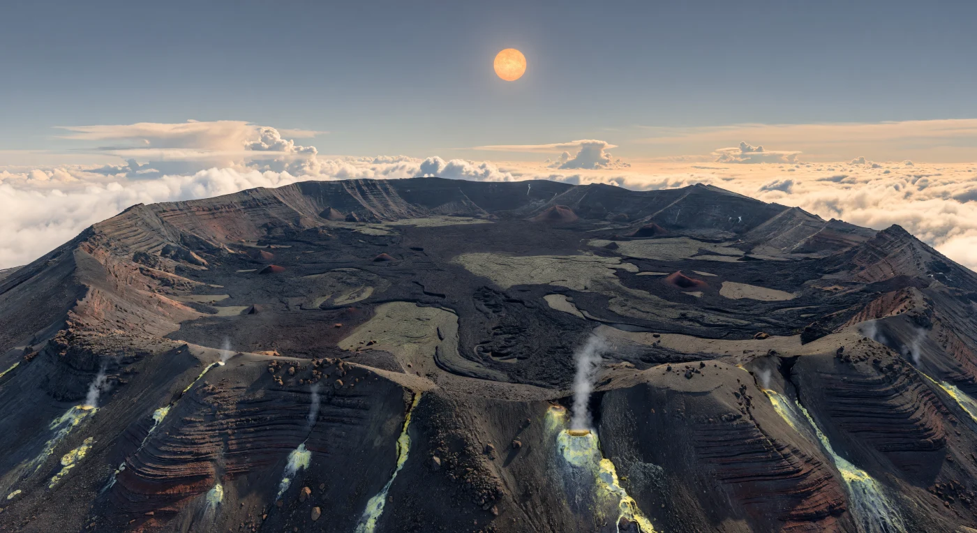 Do cume de um imenso vulcão em escudo, a paisagem abre-se para uma caldeira colapsada de escala quase inimaginável, com dezenas de quilómetros de largura, onde planícies de lava basáltica negra e recente se estendem em superfícies cordadas, campos ásperos de clínquer e lajes fraturadas salpicadas por cones de escória vermelho-acastanhados. As paredes em degraus expõem camadas de basalto escuro e cinzas oxidadas, enquanto fumarolas tingidas de enxofre libertam fios ténues de vapor branco, deixando auréolas amarelas e verde-pálidas de minerais em torno das fendas — sinais de calor interno ainda ativo num terreno moldado por vulcanismo efusivo. Muito abaixo, um oceano de nuvens brancas e creme cobre as terras baixas, realçando a altitude extrema e a gravidade algo superior deste mundo, visível nas formas largas, pesadas e compactas da paisagem. Acima dessa manta luminosa, o céu surge mais límpido, azul-acinzentado e mais claro no horizonte, onde a estrela alaranjada e branco-âmbar brilha como um disco um pouco menor que o Sol, lançando sombras nítidas e quentes sobre a rocha negra e fazendo cintilar discretamente os cristais de enxofre e o vapor.